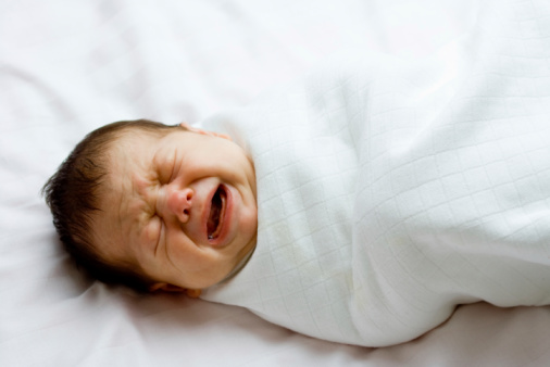 Portrait of infant baby boy crying and screaming lying on bed.