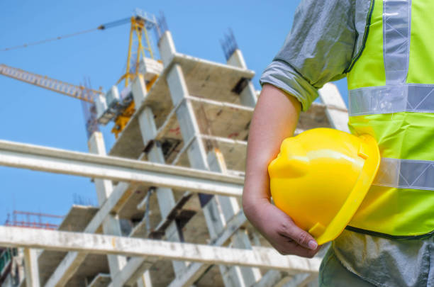 istock Close-up construction worker holding hard hat with background of blurred construction site. 969345344