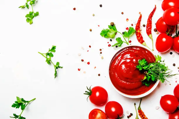 Spicy tomato ketchup sauce with herbs, chili and cherry tomatoes in bowl on white food background, top view
