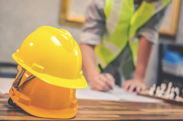 istock Yellow hard safety helmet hats for safety project of workman as engineer or worker, engineering working project blue print on the table at construction site 969360248