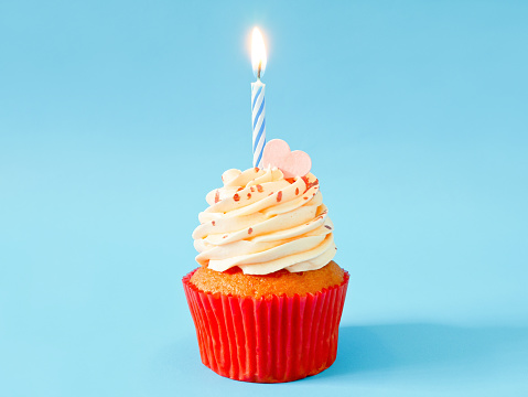 Cupcake with buttercream frosting and birthday candle on blue background with copy space