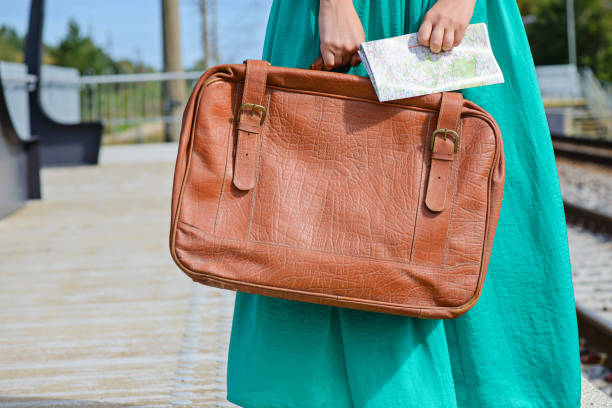 Girl in a green skirt holding a map and brown suitcase at train station