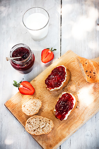 Slices of bread with homemade organic strawberry jam on a white plate at wooden table. Served with glass of fresh milk.