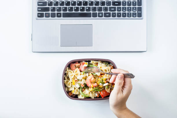 istock Container with salad with pasta in the workplace near the computer. Lunch in the office during a break between work. Woman take a food. Top view, flat lay 969414834
