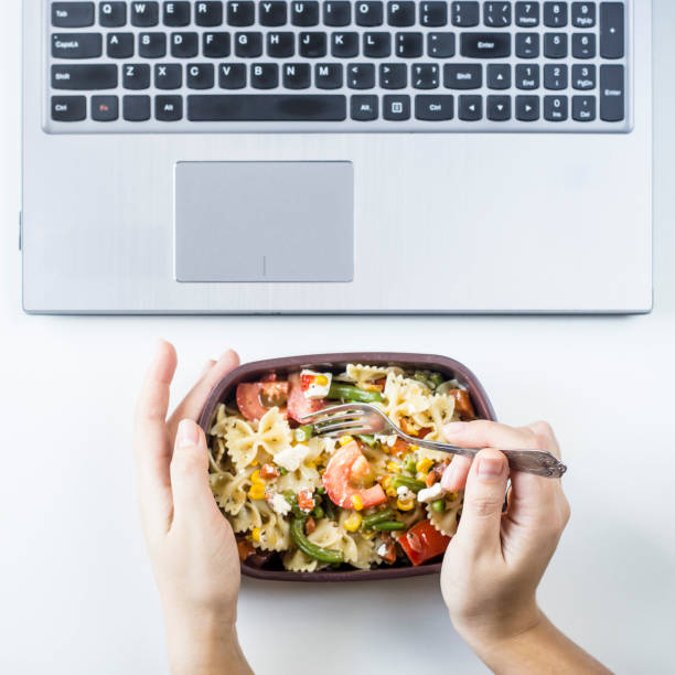istock Container with salad with pasta in the workplace near the computer. Lunch in the office during a break between work. Woman take a food. Top view, flat lay 969414846