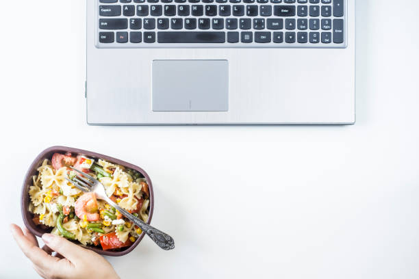istock Container with salad with pasta in the workplace near the computer. Lunch in the office during a break between work. Woman take a food. Top view, flat lay 969414848