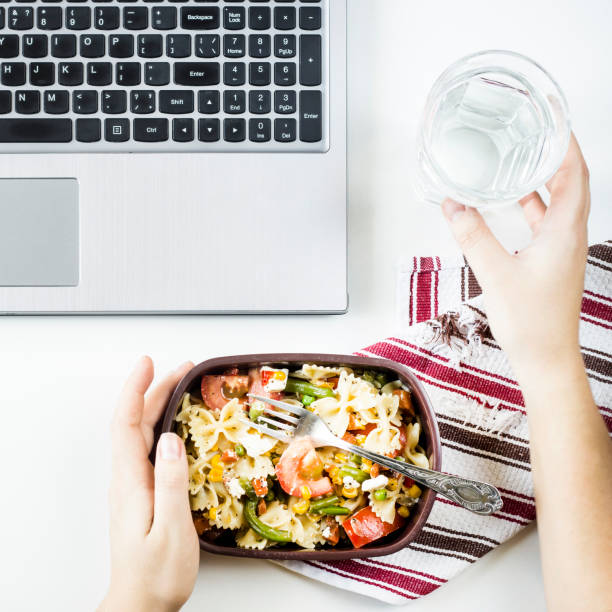 istock Container with salad with pasta in the workplace near the computer. Lunch in the office during a break between work. Woman take a food. Top view, flat lay 969414872
