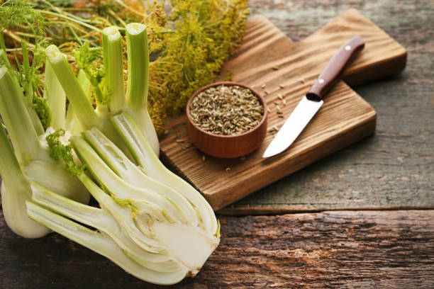 Ripe fennel bulbs and dry seeds in bowl on wooden table stock photo