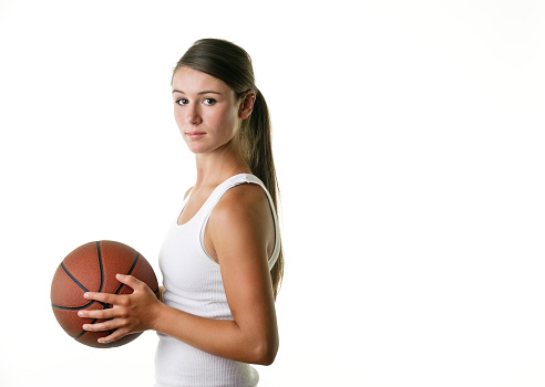 Waist up shot of a basketball player. She is holding the basketball and has a serious look on her face. Studio shot on a white background.