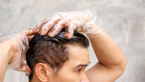 Asian men dye his hair color on a gray background.