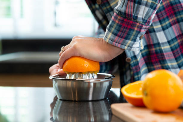 close-up of hands of a woman squeezing oranges for juice Young woman cutting oranges before squeezing them in a modern kitchen freshly squeezed stock pictures, royalty-free photos & images