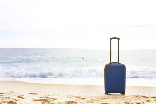 istock One hard shell suitcase on a beach. Tropical destination vacation concept. Extended telescoping luggage handle. 969473320