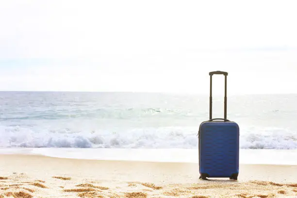 Photo of One hard shell suitcase on a beach. Tropical destination vacation concept. Extended telescoping luggage handle.