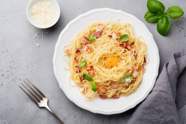 istock Pasta spaghetti carbonara with bacon, parmesan cheese, egg yolk and basil leaves on gray light background. Traditional Italian dish. Top view. 969480250