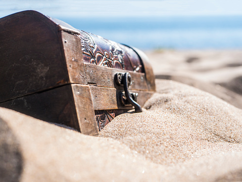 Open treasure chest full of golden coins on sandy beach. Wealth and treasure concept. 3d illustration