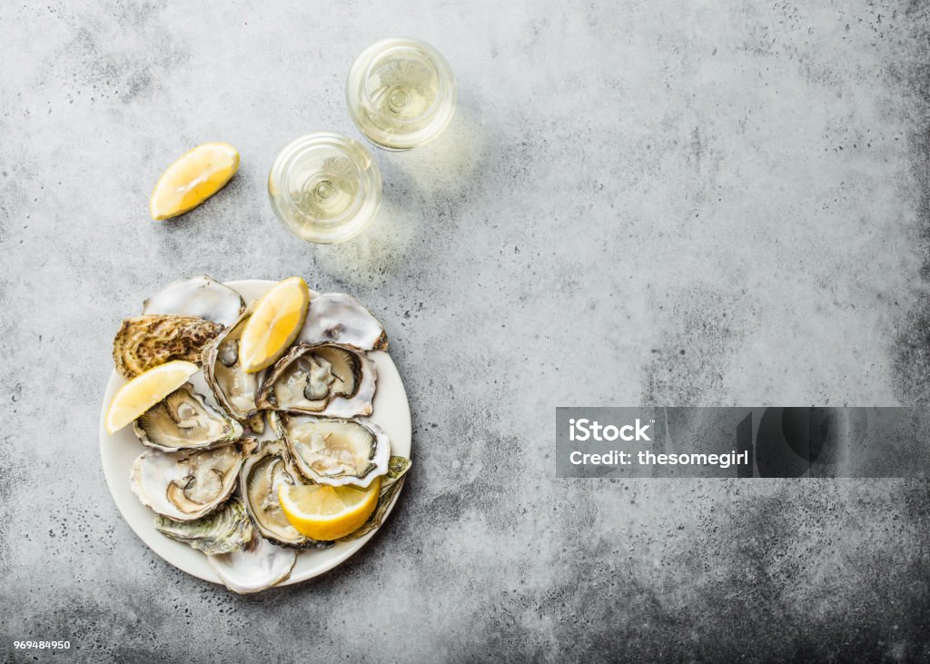 Fresh opened oysters Close-up of half dozen of fresh opened oysters and shells with lemon wedges on a plate, two glasses of white wine, top view, grey rustic concrete background, space for text Oyster Stock Photo