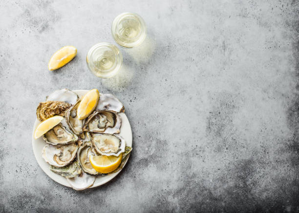 Fresh opened oysters Close-up of half dozen of fresh opened oysters and shells with lemon wedges on a plate, two glasses of white wine, top view, grey rustic concrete background, space for text oyster photos stock pictures, royalty-free photos & images