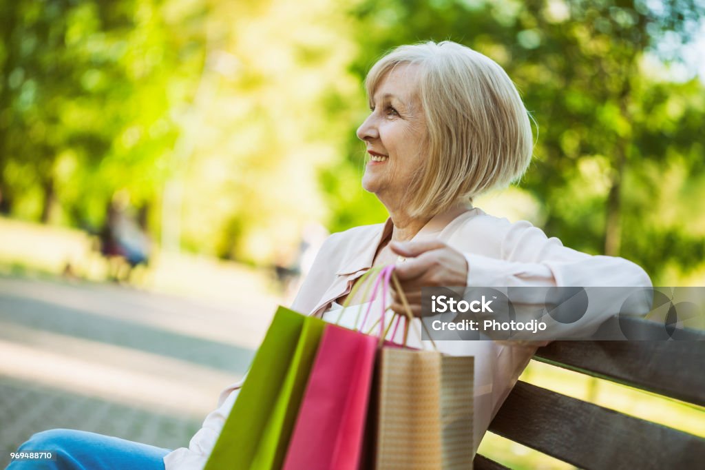 Adult woman in park Happy adult woman sitting in park after shopping. Bag Stock Photo