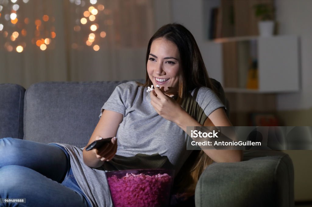 Happy woman watching tv in the night at home Happy woman watching tv in the night sitting on a couch in the living room at home Watching TV Stock Photo