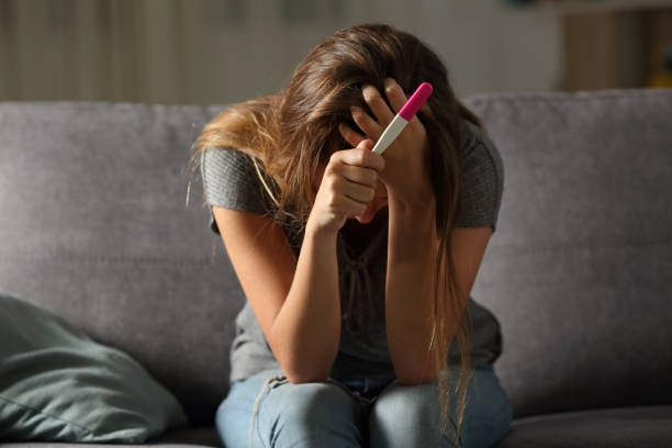 Sad woman complaining holding a pregnancy test Single sad woman complaining holding a pregnancy test sitting on a couch in the living room at home unwanted pregnancy stock pictures, royalty-free photos & images