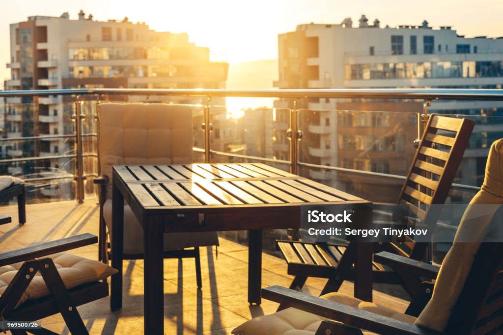 Outdoor Terrace With Garden Furniture In The Background Of The City And Sunset. Luxury Apartments Resort Recreation Summer Concept Outdoor Terrace With Garden Furniture In The Background Of The Urban And Sunset. Luxury Apartments Resort Recreation Summer Concept Balcony Stock Photo