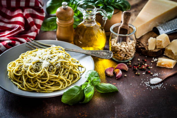 Spaghetti al pesto Genoese plate shot on dark kitchen table. Ingredients for preparing pesto sauce like olive oil, pine nuts, basil leaves, salt, pepper, garlic and Parmesan cheese are around the plate. Low key DSRL studio photo taken with Canon EOS 5D Mk II and Canon EF 100mm f/2.8L Macro IS USM