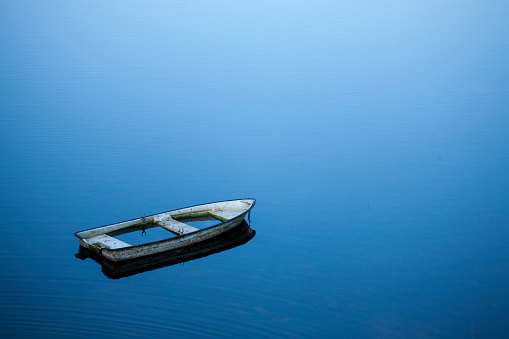 sunken abandoned rowboat in large lake with quiet water