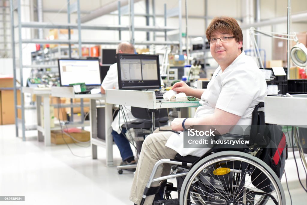 handicapped worker in a wheelchair assembling electronic components in a modern factory at the workplace Disability Stock Photo