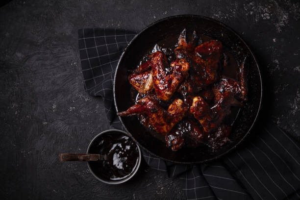 istock Chicken wings in thick barbecue sauce with garlic on black cast iron pan on dark rustic background. 969522102