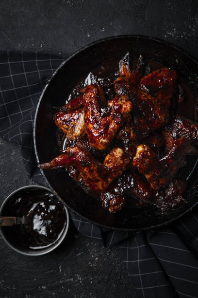 istock Chicken wings in thick barbecue sauce with garlic on black cast iron pan on dark rustic background. 969522110