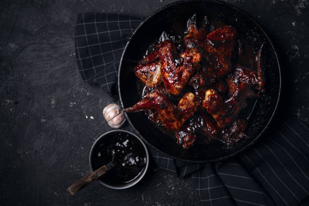 istock Chicken wings in thick barbecue sauce with garlic on black cast iron pan on dark rustic background. 969522112