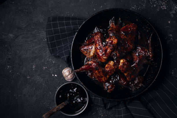 istock Chicken wings in thick barbecue sauce with garlic on black cast iron pan on dark rustic background. 969522118