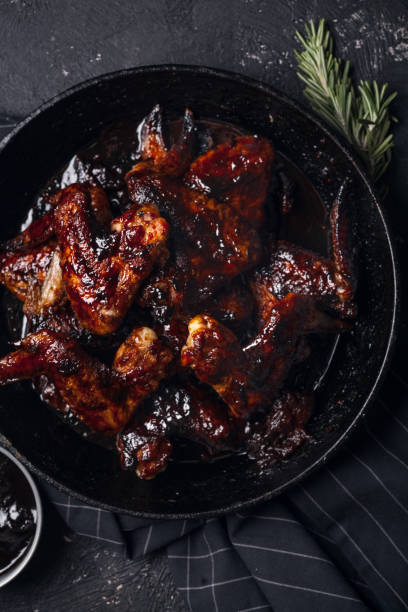 istock Chicken wings in thick barbecue sauce with garlic on black cast iron pan on dark rustic background. 969522122