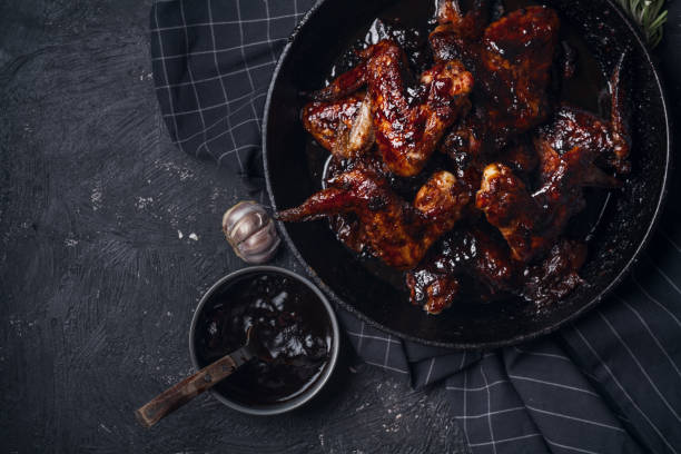 istock Chicken wings in thick barbecue sauce with garlic on black cast iron pan on dark rustic background. 969522128