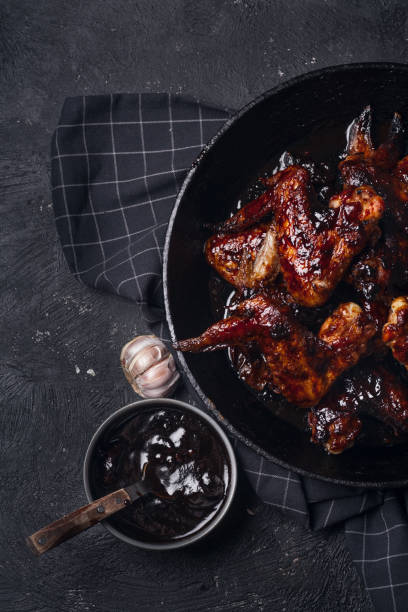 istock Chicken wings in thick barbecue sauce with garlic on black cast iron pan on dark rustic background. 969522130