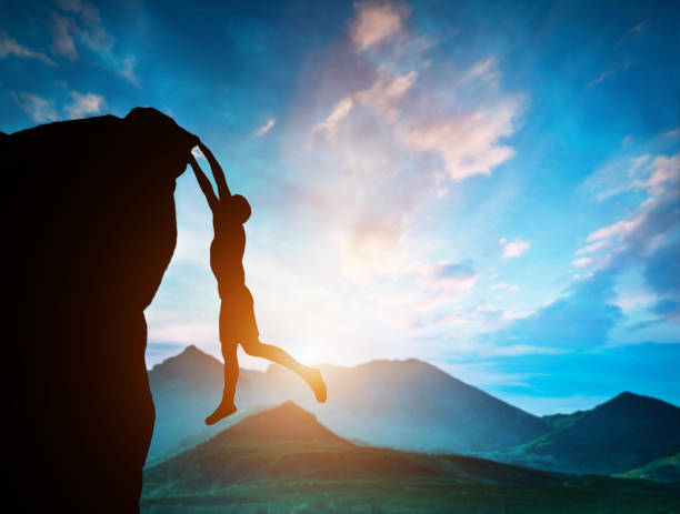 istock Man hanging on the edge of mountain at sunset 969522672