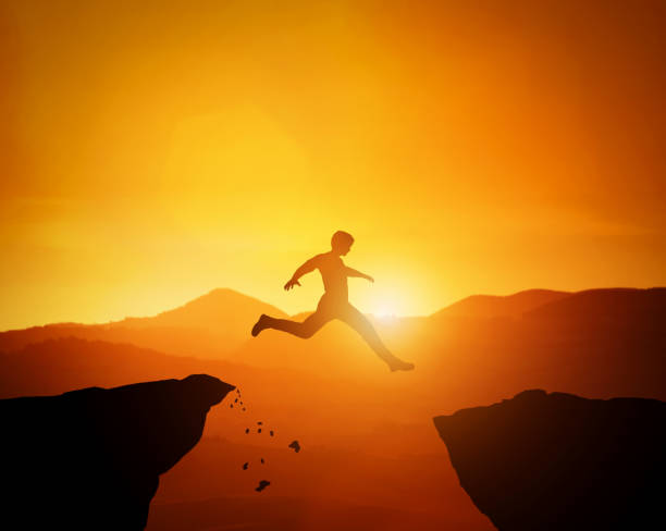 istock Man jumping from one rock to another. Sunset mountains scenery 969522674