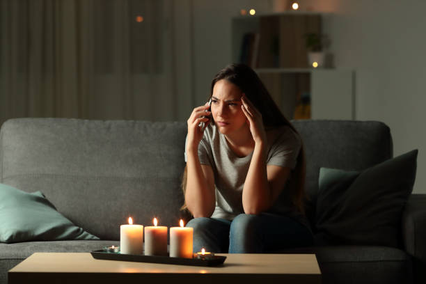 Worried woman talking on phone during blackout Worried woman talking on phone during blackout sitting on a couch in the living room at home waiting telephone on the phone frustration stock pictures, royalty-free photos & images