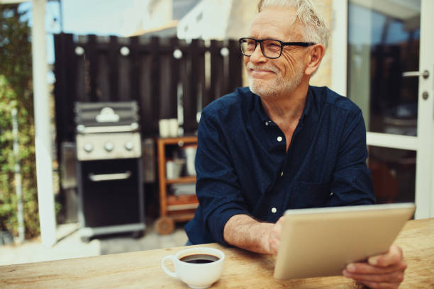 istock Smiling senior man sitting outside with a coffee and tablet 969574706