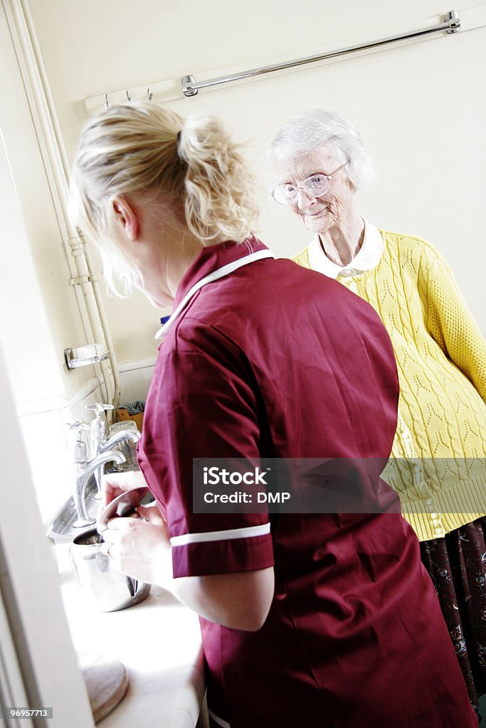 Giovane infermiera che tè per donna anziana in una casa di cura - Foto stock royalty-free di Accudire