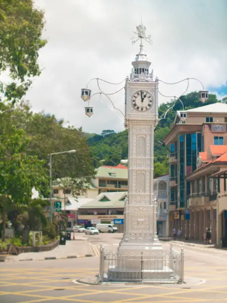 Victoria Clock Tower in Victoria, Seychelles. Viewed from the street with rural jungle covered hills in background.
