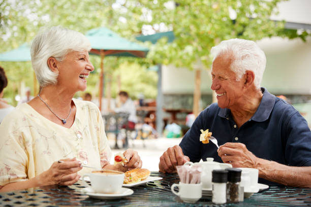 ritratto di coppia senior che si gode il pasto al bar all'aperto - 60s senior adult breakfast cheerful foto e immagini stock