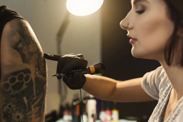Young woman tattooist doing tattoo on shoulder Concentrated woman tattooist doing tattoo with tattoo machine on male shoulder. Unusual female profession, copy space shoulder tattoo designs for men stock pictures, royalty-free photos & images