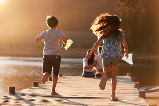 Children Run Towards Parents On Wooden Jetty By Lake