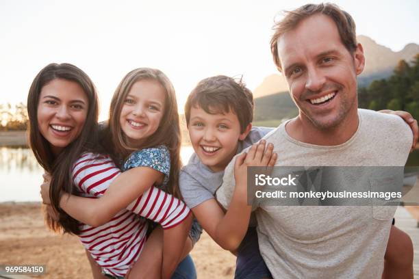 Portrait Of Parents Giving Children Piggyback Ride In Countryside Stock Photo - Download Image Now