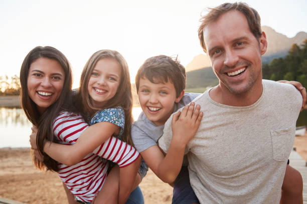 portrait of parents giving children piggyback ride in countryside - family white family with two children cheerful imagens e fotografias de stock