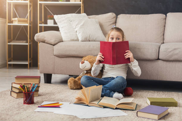 istock Little female child reading book while sitting on the carpet 969594768