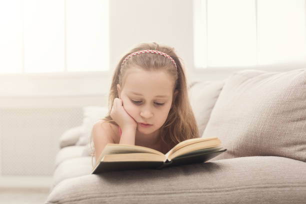 istock Pretty girl reading book, lying on sofa at home 969603324