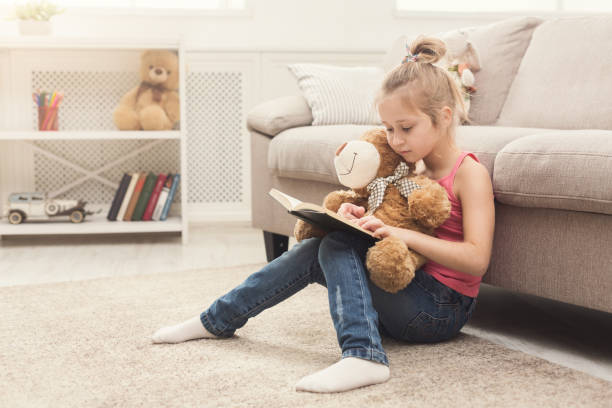 istock Lttle girl and her teddy bear reading book 969603458