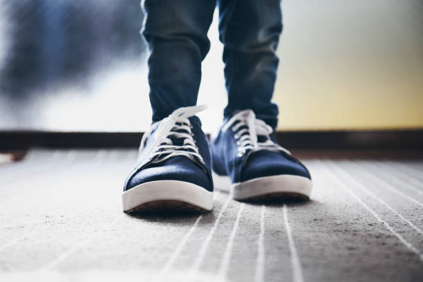 Legs of boy wearing shoes for adult at home.